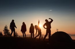 silhouette-group-people-have-fun-top-mountain-near-tent-sunset_146671-18470